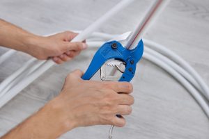 Plumber cuts a piece from a plastic pipe using a pipe cutter with a ratchet mechanism in close-up